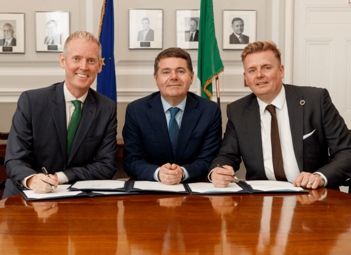 Andrew McDowell, Paschal Donohoe and Barry Napier sit at a table and sign a document together.