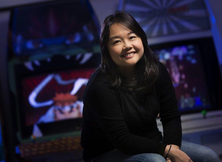 Elicia Lee in a black jumper smiling with arcade machines in the background.