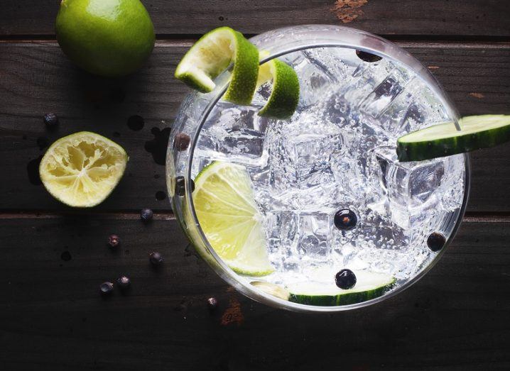 Birdseye view of a glass of gin with a lime with ice on a wooden table.