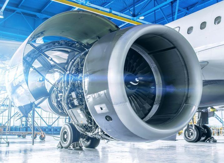 Close-up of a jet engine with side panel open for examination in a large aircraft hangar.