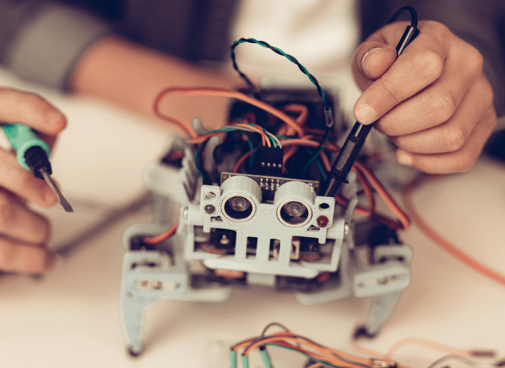 A child's hands building a small robot and holding tools.