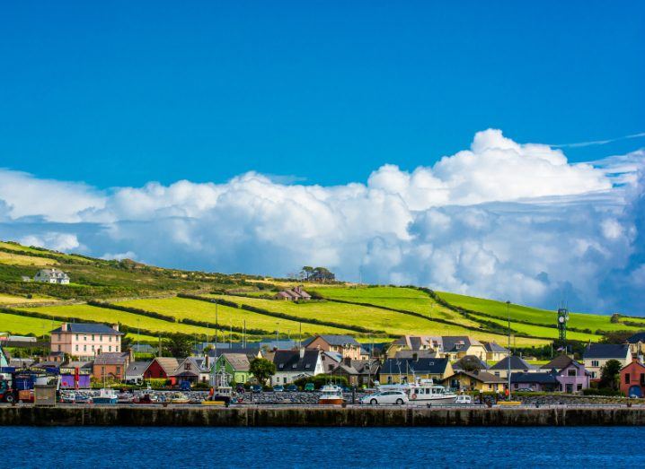 The coastline of Dingle town in Kerry, with green hills rising in the background and a blue sky above.