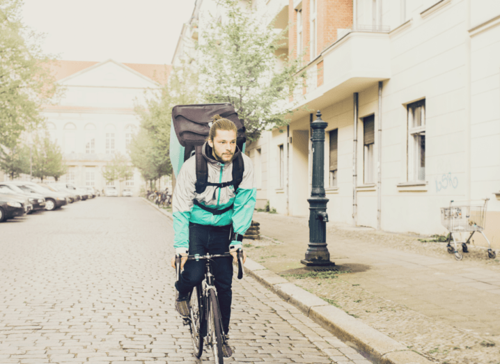 A Deliveroo cyclist cycles up a cobble-stoned street in a city.