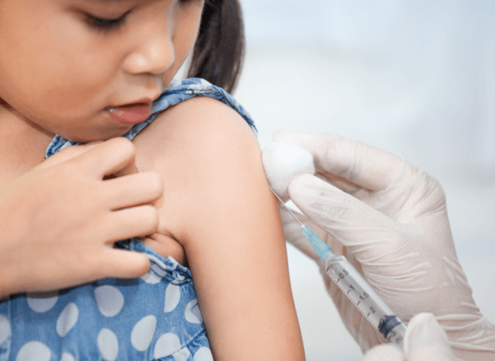 A child in a blue polka dot vest gets a vaccination from a medical professional.