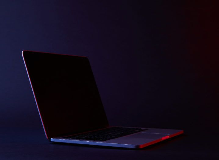 View of turned off sleek laptop with metal chassis in room with dark purple walls and floor, bathed in red light.