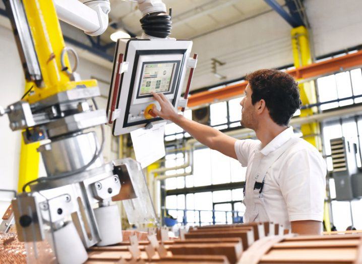 A young male mechanical engineer operates a machine for winding copper wire to manufacture transformers in a factory.