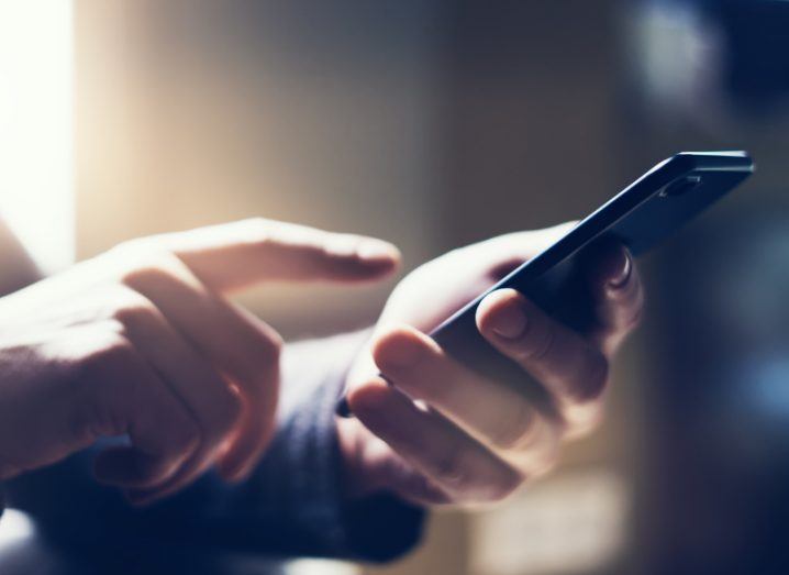 View of hands holding a smartphone in a room with sunlight streaming through window.