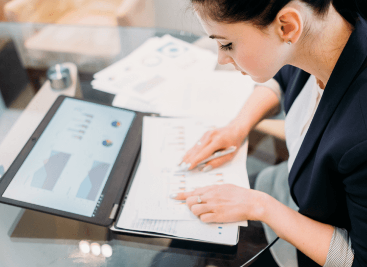 A woman wearing a navy blazer sitting at a desk studying report papers with graphic data results.