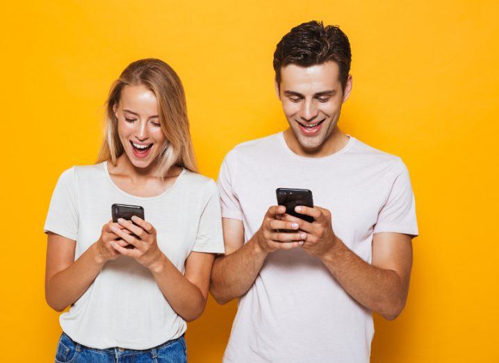 View of couple wearing matching white T-shirts smiling down at their phones while using apps.