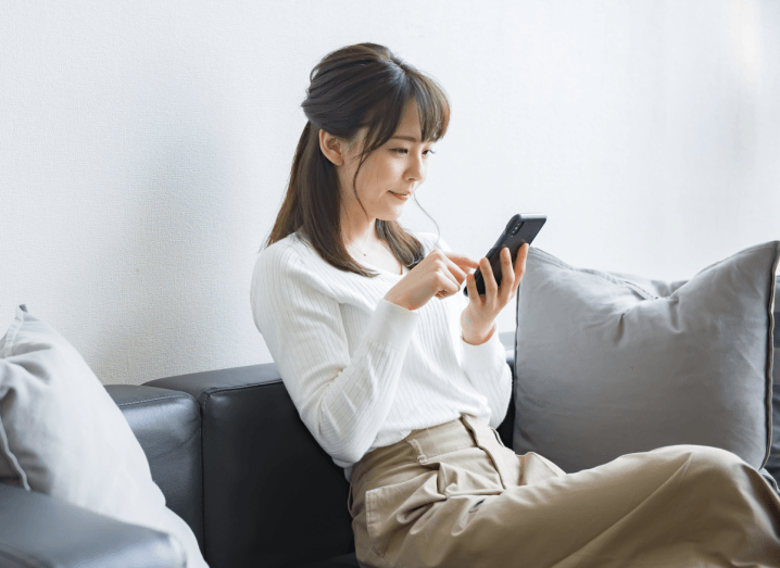 A woman looking at an iPhone on a sofa.