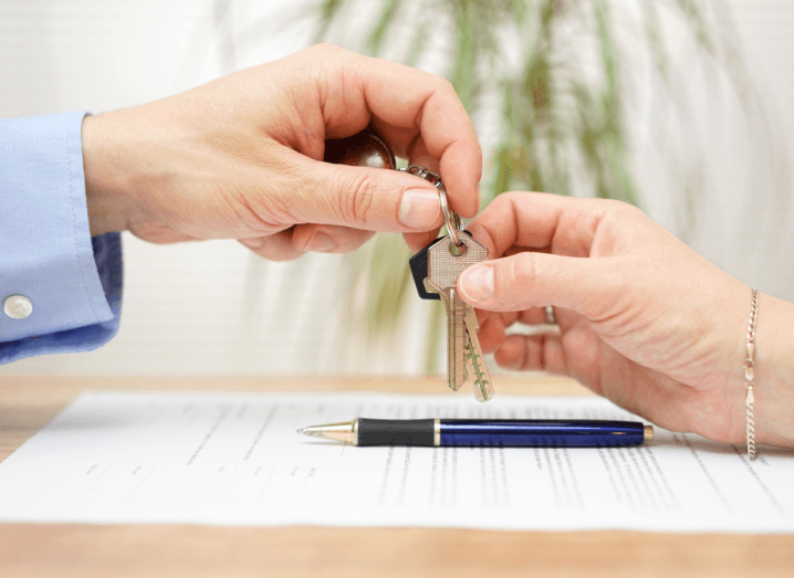 A landlord exchanging keys to a tenant over a contract and pen.