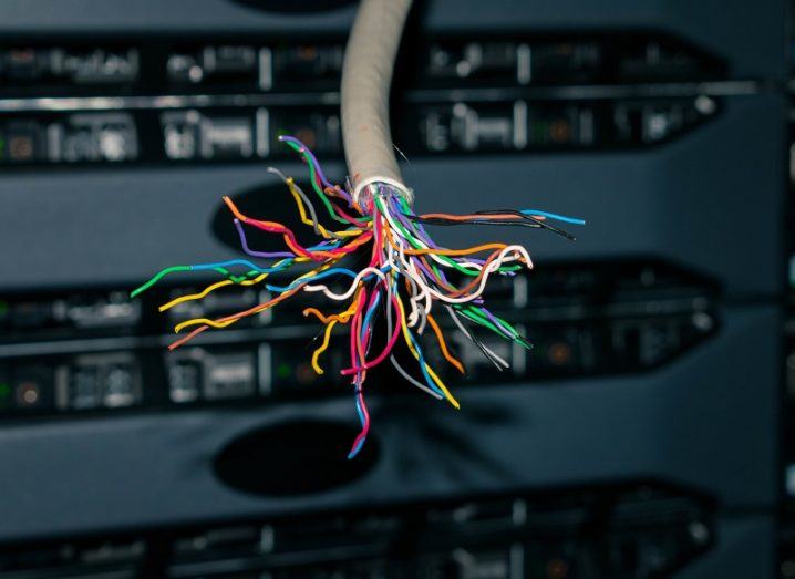 Internet cable ripped apart with loose inner wires splayed against a computer unit background.