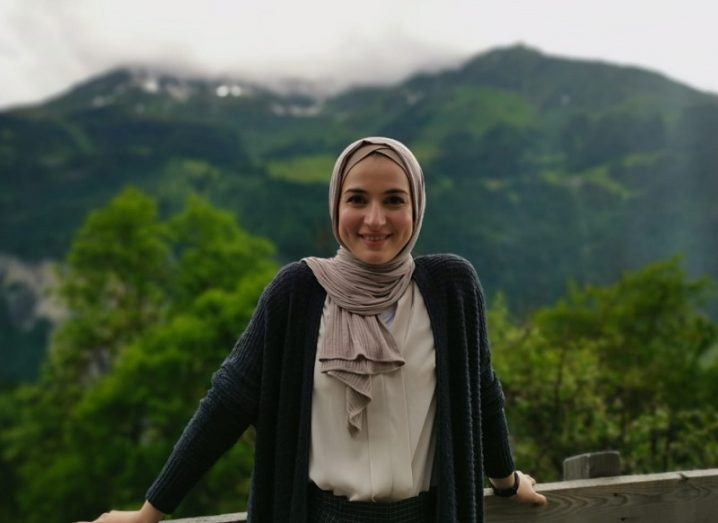 Dr Deema Almasri smiling in a cardigan against a backdrop of forest and mountains.