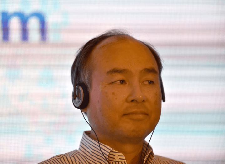 SoftBank's CEO, a man in his sixties, wearing headphones and sitting in front of a large white screen.
