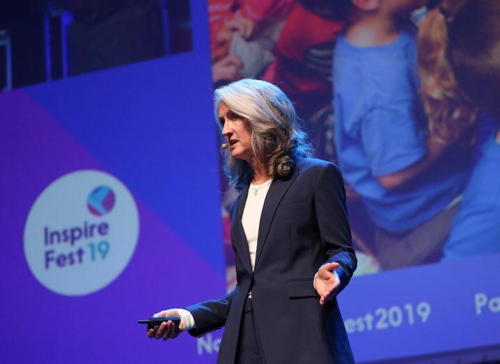 Rafferty Jackson, a woman with white hair and a dark suit, stands on the stage at Inspirefest 2019