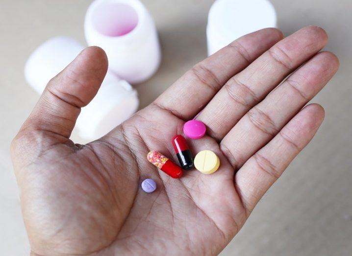 Hand holding a bunch of multicoloured pills with medicine bottles in the background.