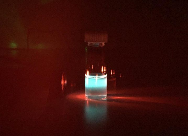 A vial of nanoparticles coloured blue with an infrared light being shone into it against a black background.