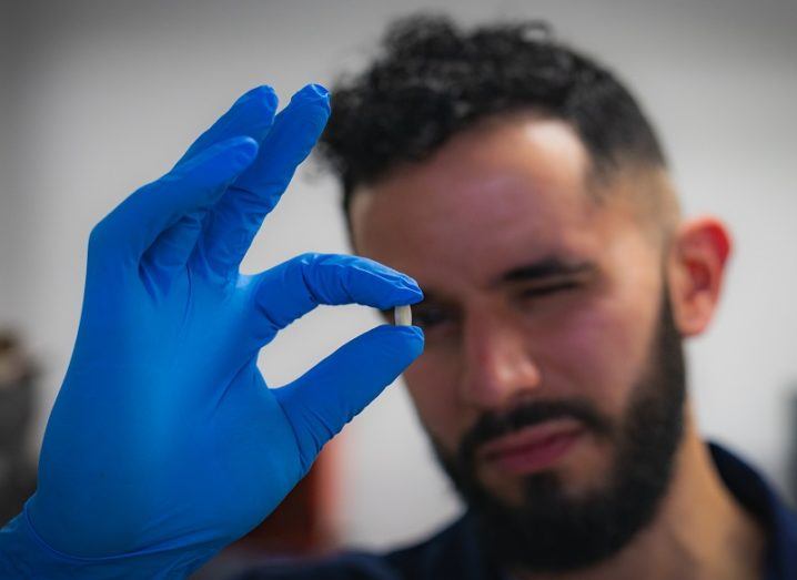 Evert Feunmayor, a bearded young man wearing a blue glove, holding the pill up to the camera.
