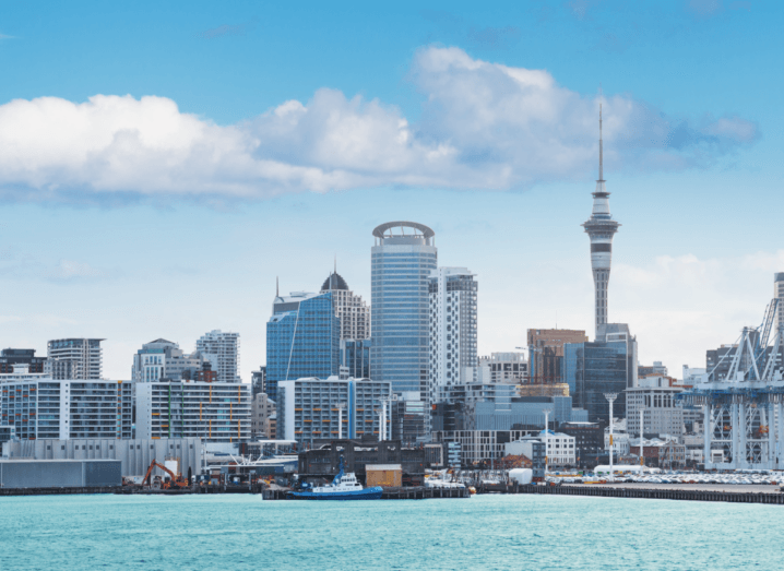 Auckland's skyline, featuring tall buildings in front of a clear blue sky and a calm blue ocean.