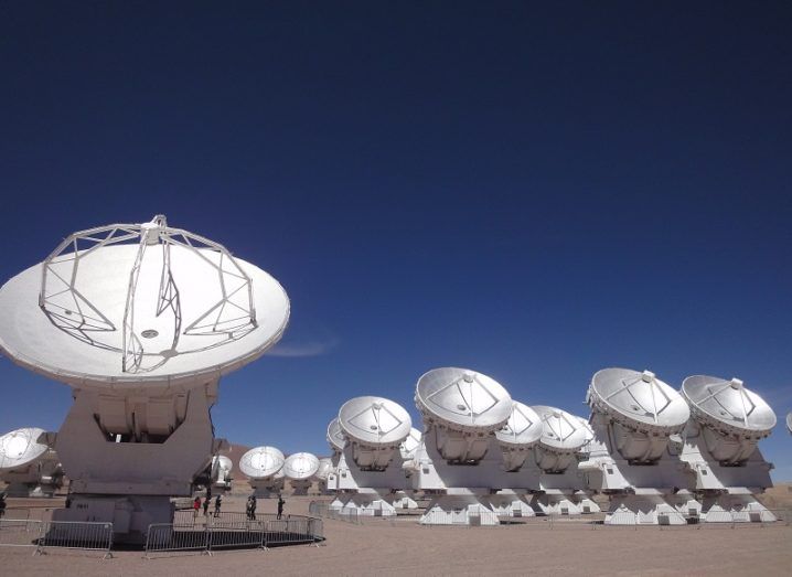 Series of radio telescope dishes pointing to the sky against a darkening sky.