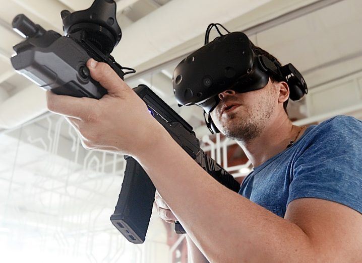 Person wearing a VR headset and holding a VR rifle while playing a video game.