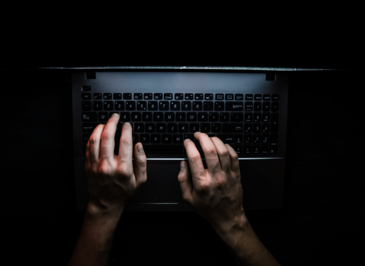 A person typing on a laptop in the dark.