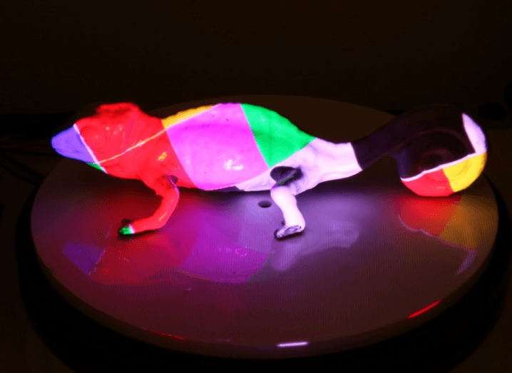 A chameleon figure with illuminous PhotoChromeleon colours in a dark room.
