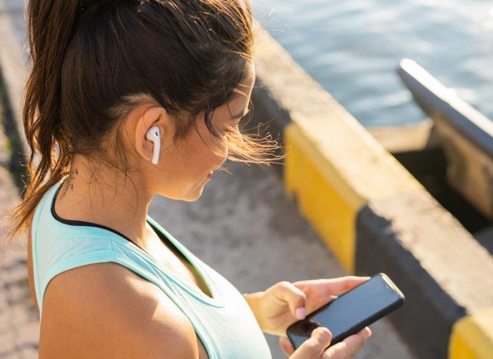 Woman wearing fitness clothes using an earbud and holding a phone.