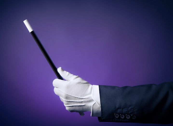 Magician's hand with white glove holding a magic wand.
