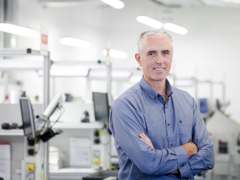 Man standing in laboratory with arms folded, wearing blue shirt.