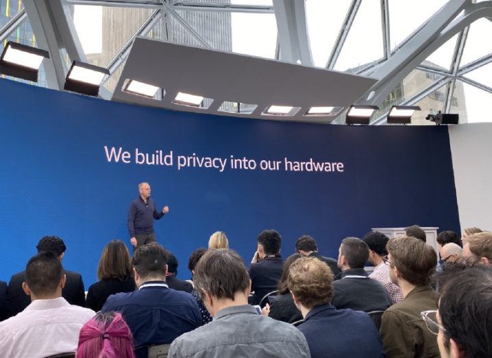 A man speaks to an audience gathered at Amazon’s Seattle headquarters in front of a backdrop that says: “We build privacy into our hardware”.