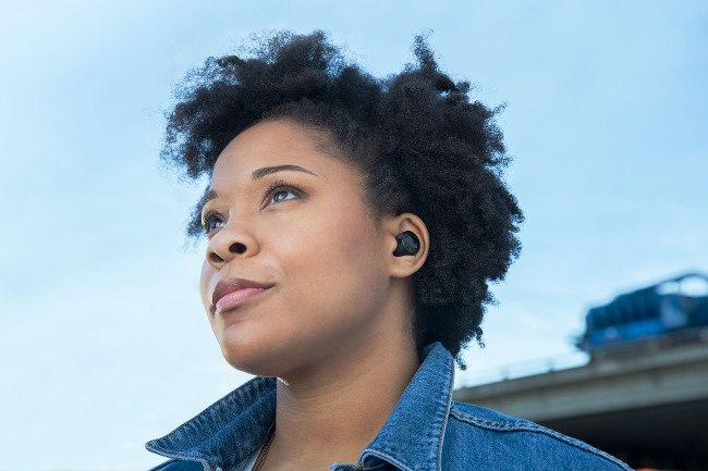 A woman in a denim shirt pictured wearing the black Echo Buds in her ears.