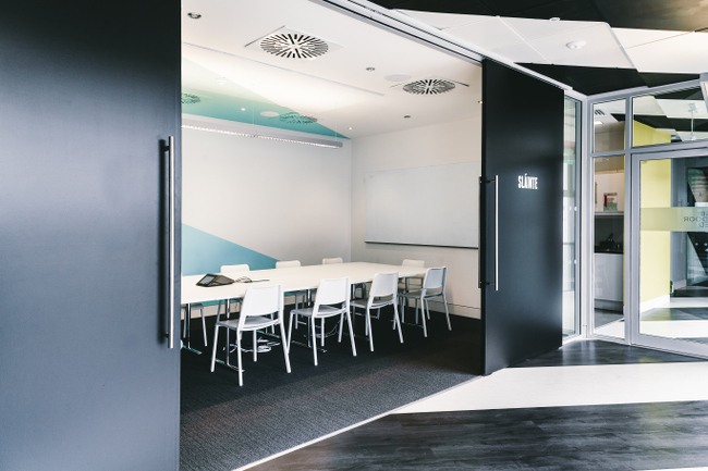 Two moving walls slide apart to show a boardroom inside with a long white table surrounded by white chairs