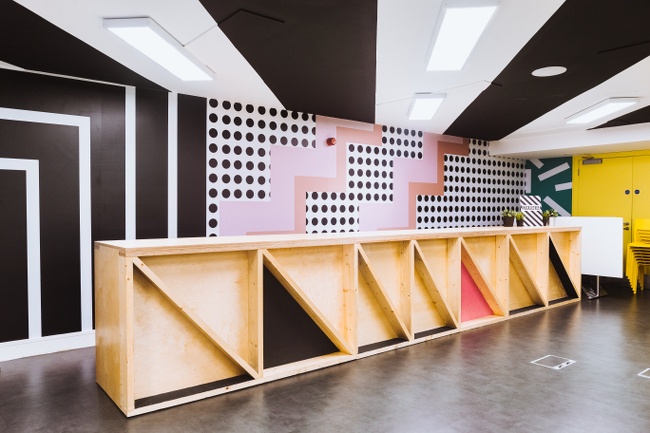 A brightly coloured room (black, white and pink) with a wooden fold-away stage.