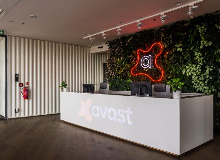 View of front desk of modern office with Avast logo rendered in neon on wood panelling.