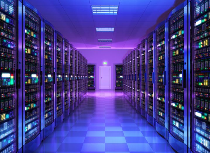 A hallway flanked with data servers lit up with multi-coloured lights all bathed in purple electric haze.