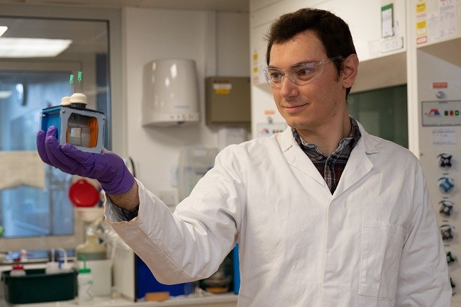 Scientist Virgil Andrei in a white lab coat holding an artificial leaf in a lab.