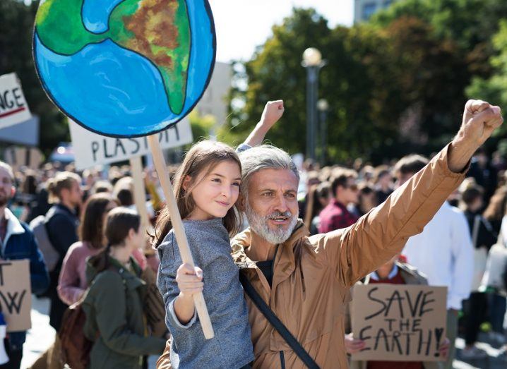 Young child holding a sign during a climate protest held up by a man with a white beard and brown jacket.