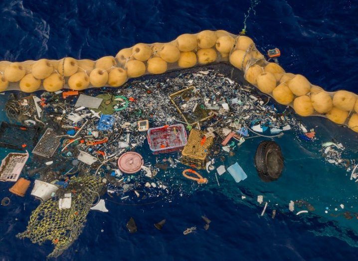 Floating pile of plastic in the ocean captured by a large, yellow capture system.