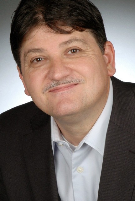 View of man in business suit with grey moustache and brown hair.