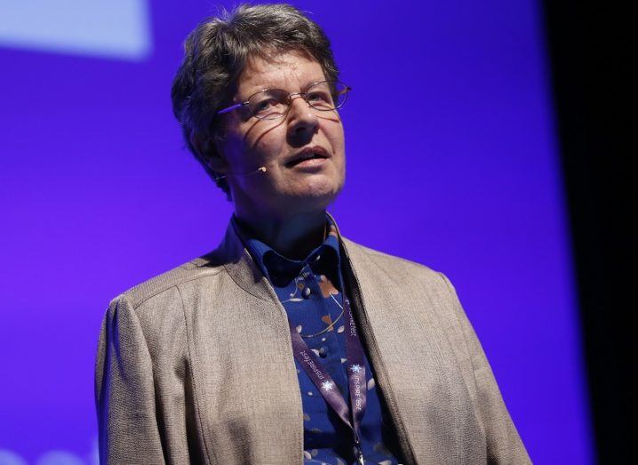 Jocelyn Bell Burnell speaking on stage at Inspirefest 2015 in a beige jacket and purple shirt against a purple background.