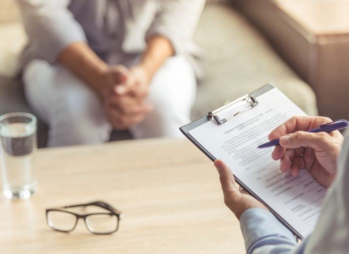 Image of a psychiatrist holding a clipboard and pen with a patient on a couch.