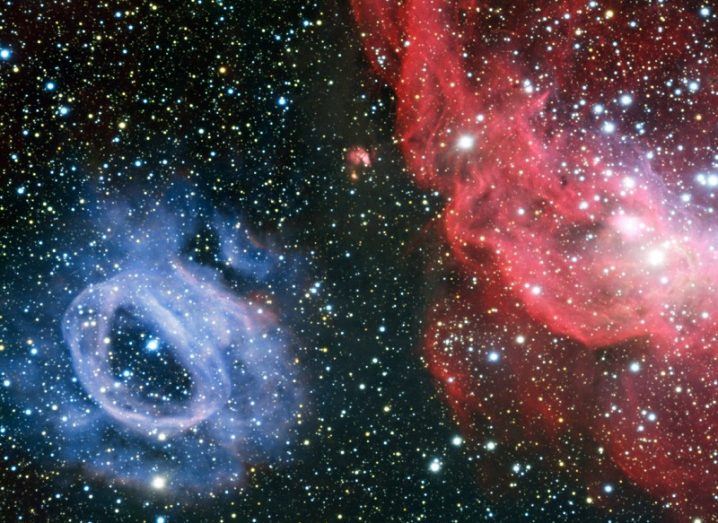 A red and blue cloud of cosmic gas orbiting one another against a starry background.