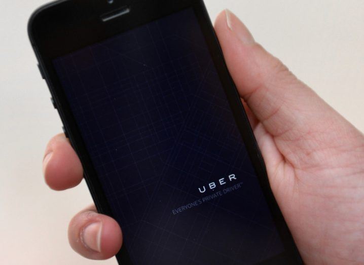 View of Uber app on black smartphone in someone's hand against beige background.
