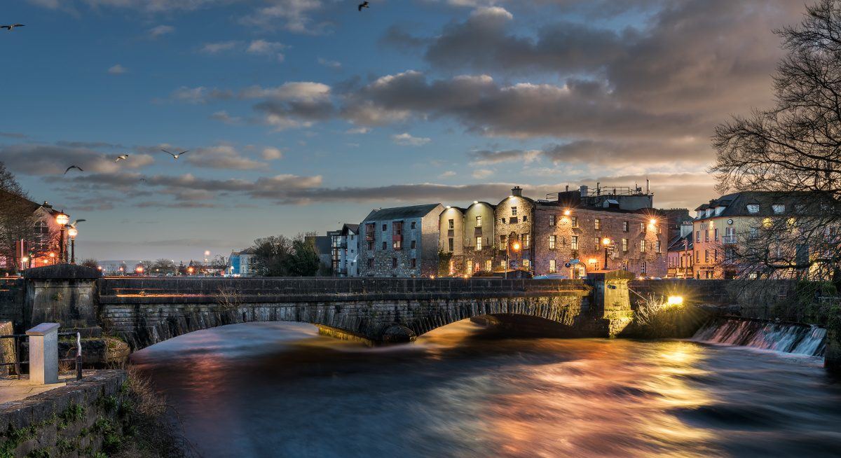 Sunset over Galway's Bridge Mills, with light reflecting on a river.