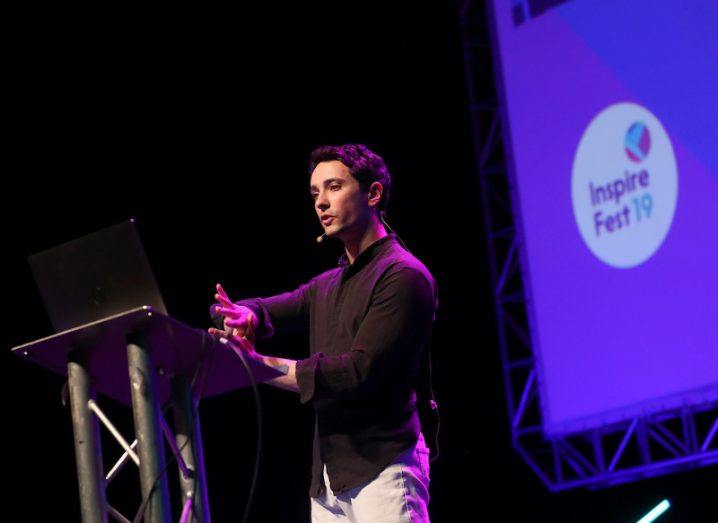 A man in a black shirt stands on stage in front of a screen that reads, Inspirefest 2019.