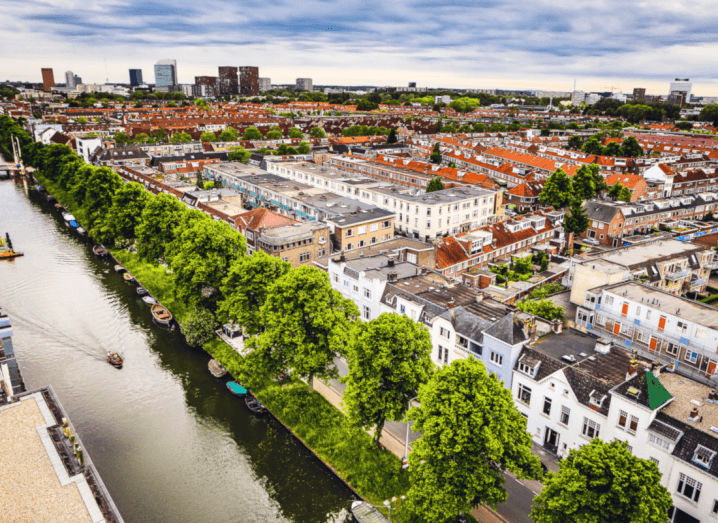 A view from above the city of Utrecht. A canal lined by trees is visible in front of rows and rows of traditional Dutch-style buildings.