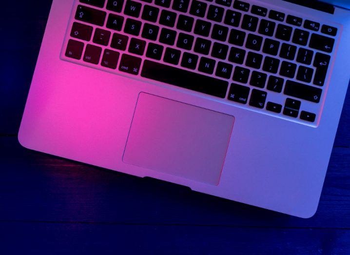 Laptop computer keyboard on wood office desk table at night with blue lights shining over the keyboard.