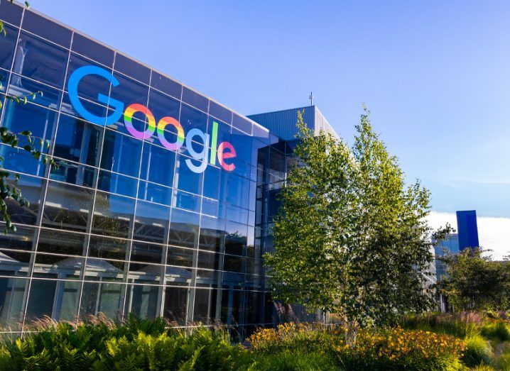 Sunny day with view of glass façade of office building with multi-coloured Google logo on top of building.