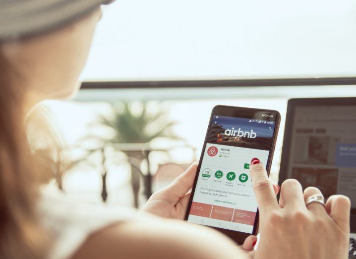 View of woman in sunhat holding up smartphone while using Airbnb app.